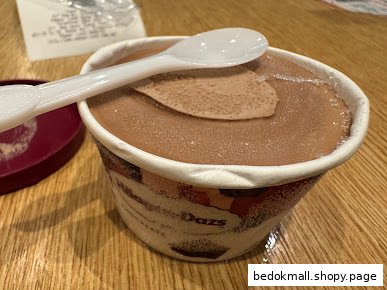 A cup of chocolate ice cream with a white spoon on a wooden table.