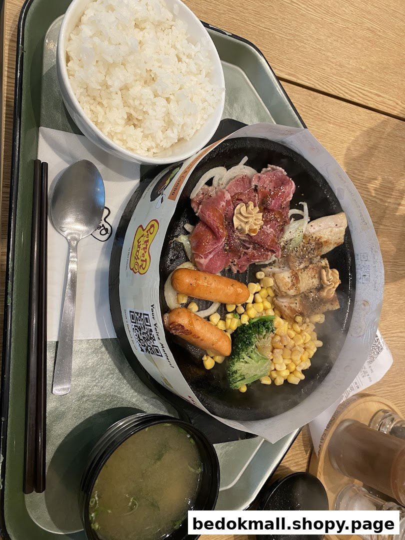 A hot plate meal with meat, sausages, vegetables, rice, and soup on a tray.