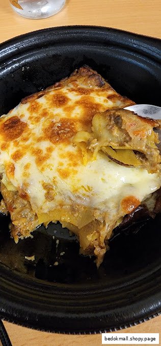 Close-up of a cheesy, layered dish in a black bowl with a spoon.
