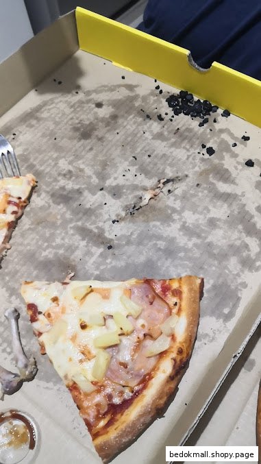A pizza box with a slice of pizza, chicken bone, and sauce.