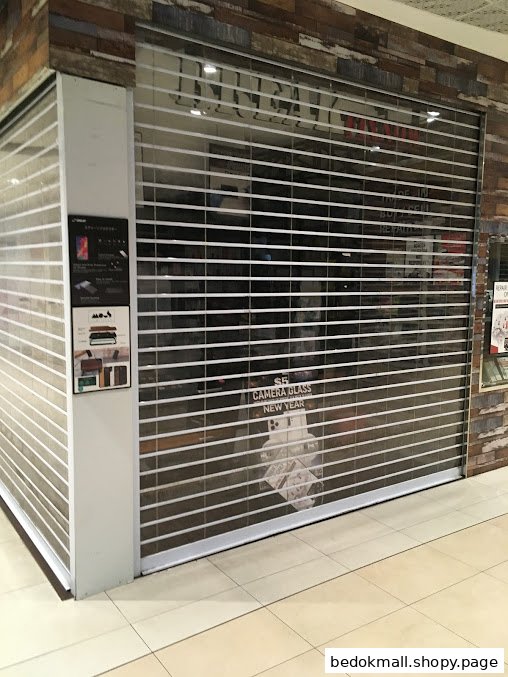 Closed shop front with security shutter and promotional signs visible through glass.