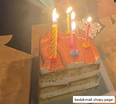 A tiramisu-style cake with several lit birthday candles on top.