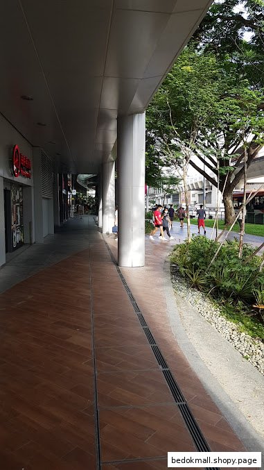 View of an outdoor mall walkway with shops, pillars, and trees.