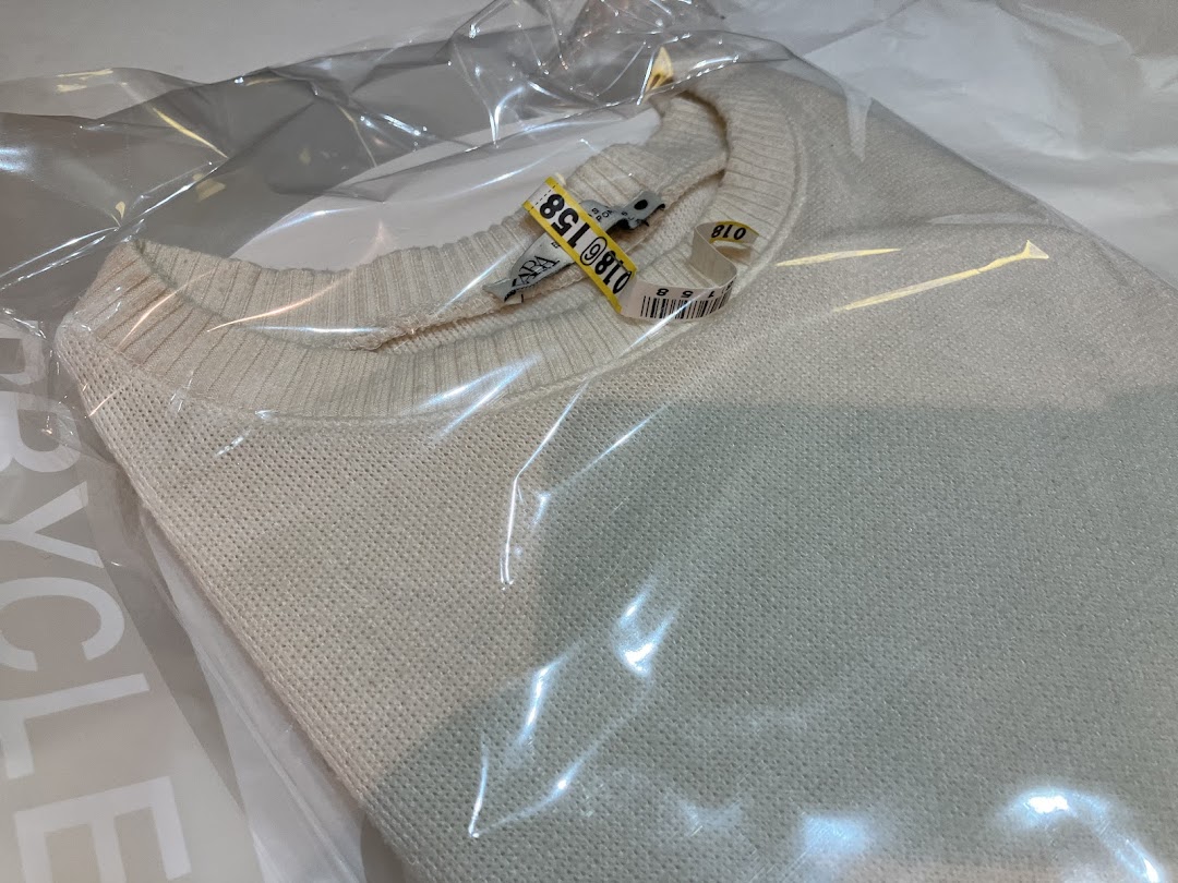 A light-colored sweater in a plastic dry cleaning bag with tags.