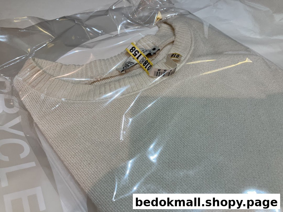 A light-colored sweater in a plastic dry cleaning bag with tags.