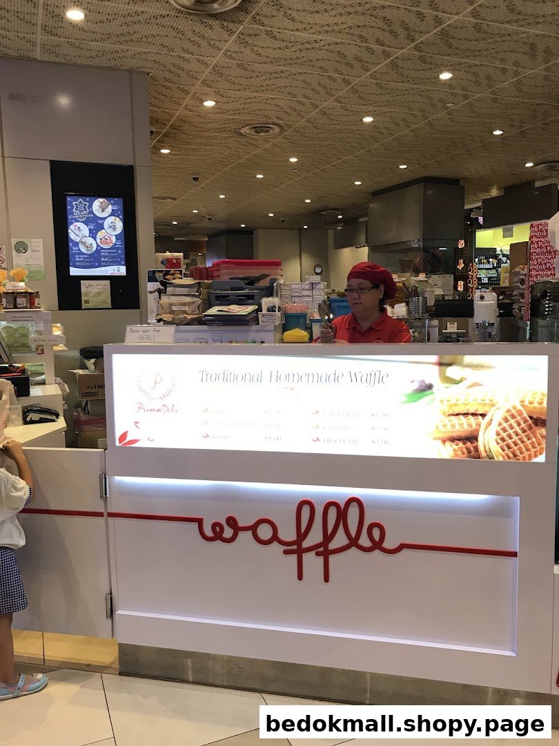 Interior view of a PrimaDéli shop with a staff member and waffle counter.
