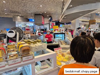 Interior view of a bakery counter with baked goods, staff, and customers.