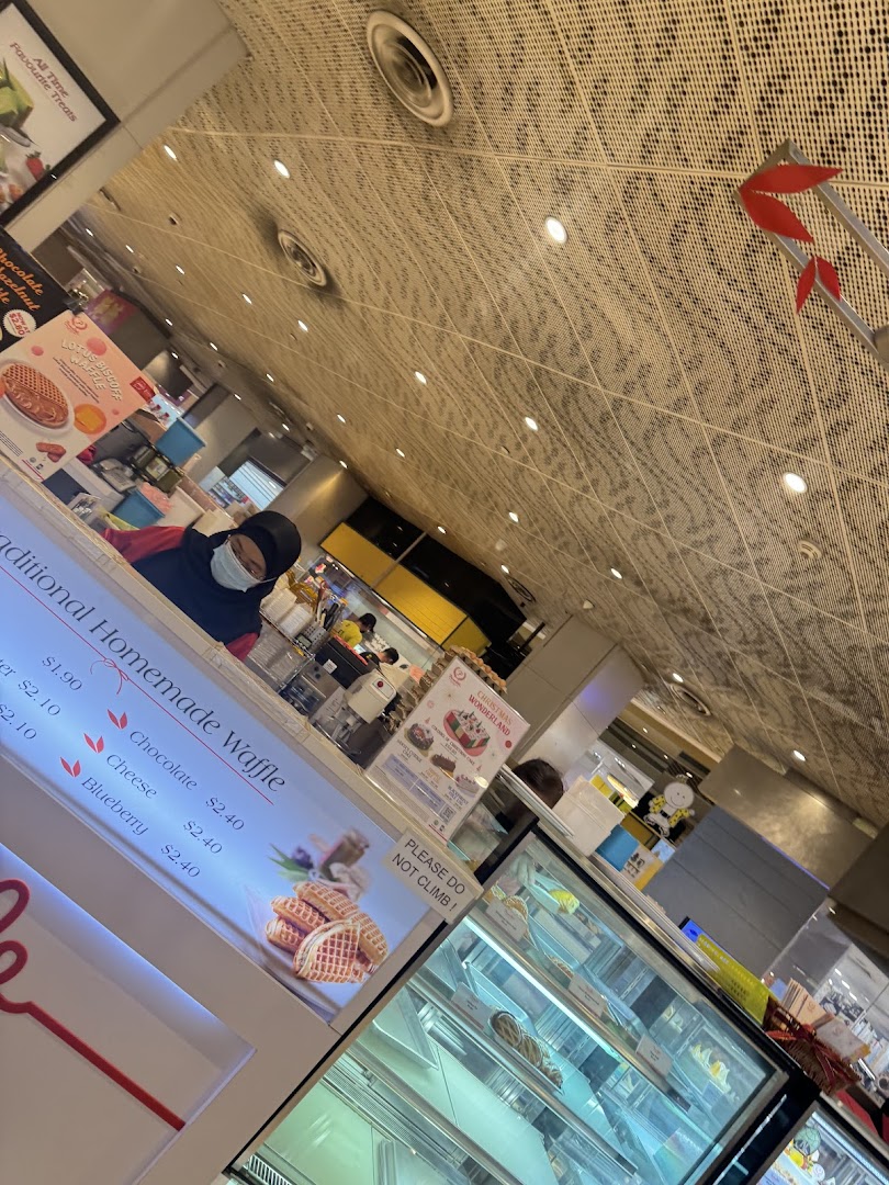 Interior view of a shop counter with a staff member, display cases, and a waffle menu.