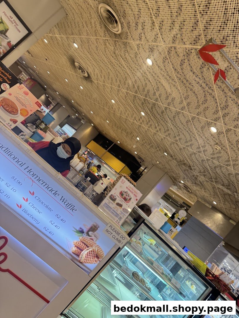 Interior view of a shop counter with a staff member, display cases, and a waffle menu.