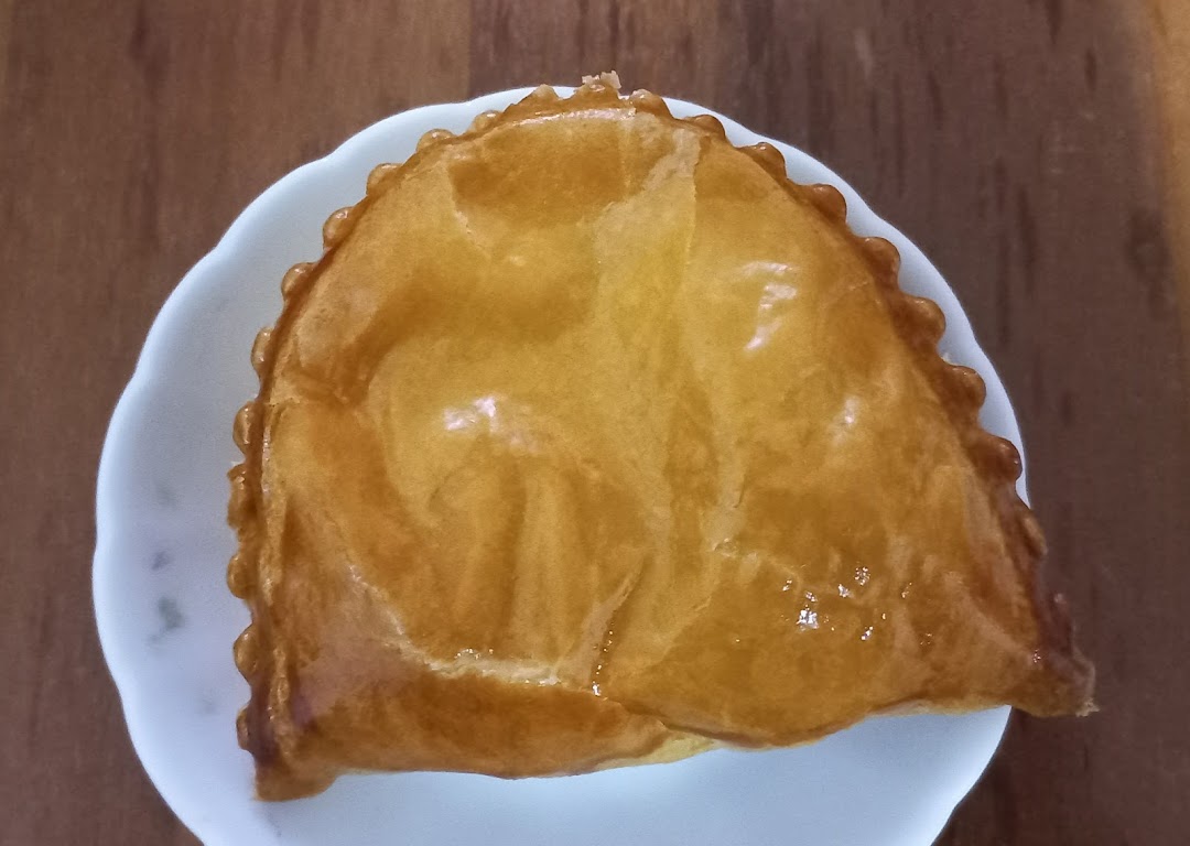 A golden-brown pastry, possibly a curry puff, on a white plate.