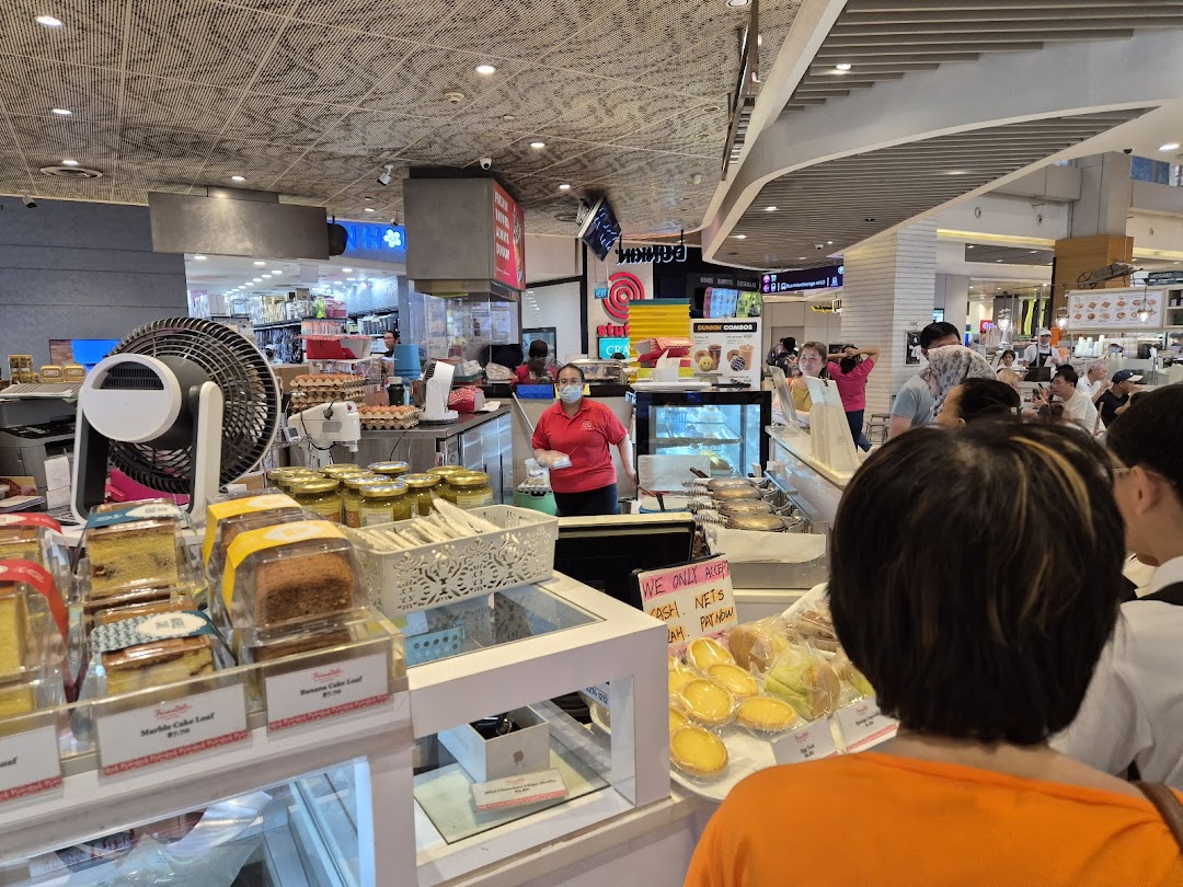 Interior view of a bakery counter with cakes, tarts, staff, and customers.