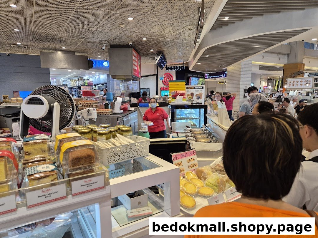 Interior view of a bakery counter with cakes, tarts, staff, and customers.