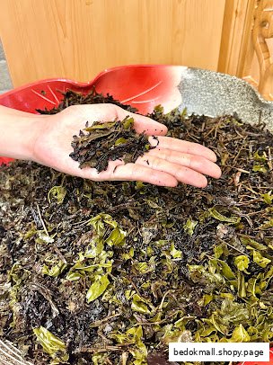 A hand holds dried tea leaves over a large pile of the product.