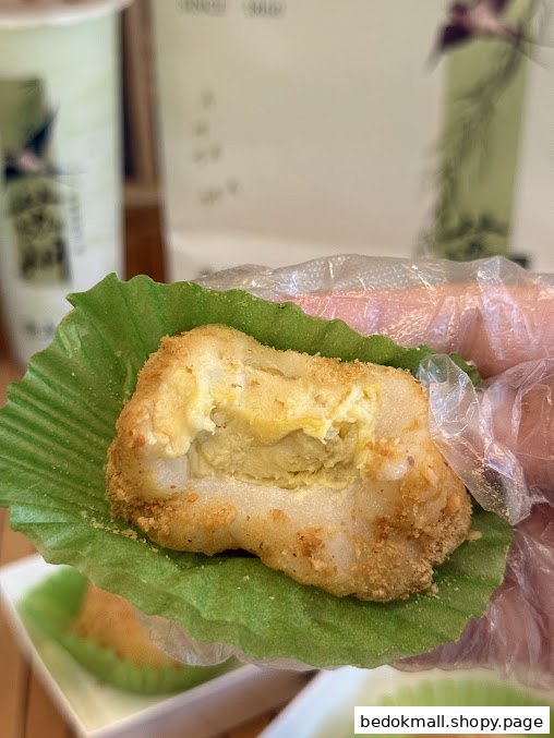 Hand holding a dessert with creamy filling in a green paper liner.