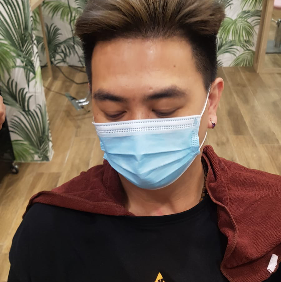 A person wearing a face mask and a red cape in a hair salon.