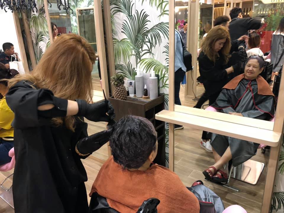 A stylist colors a client's hair inside a busy hair salon.