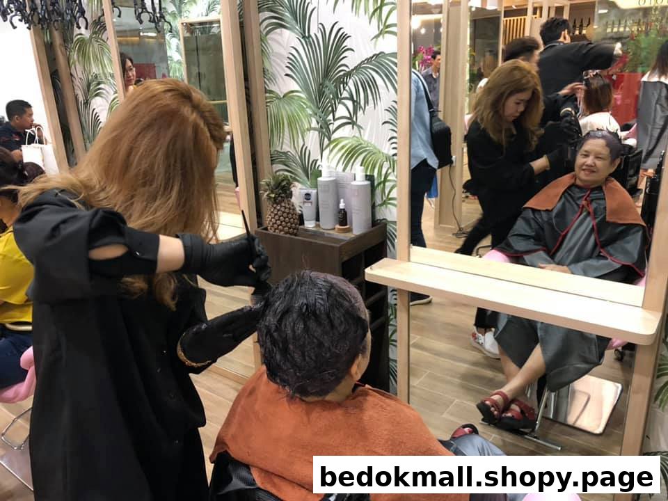 A stylist colors a client's hair inside a busy hair salon.