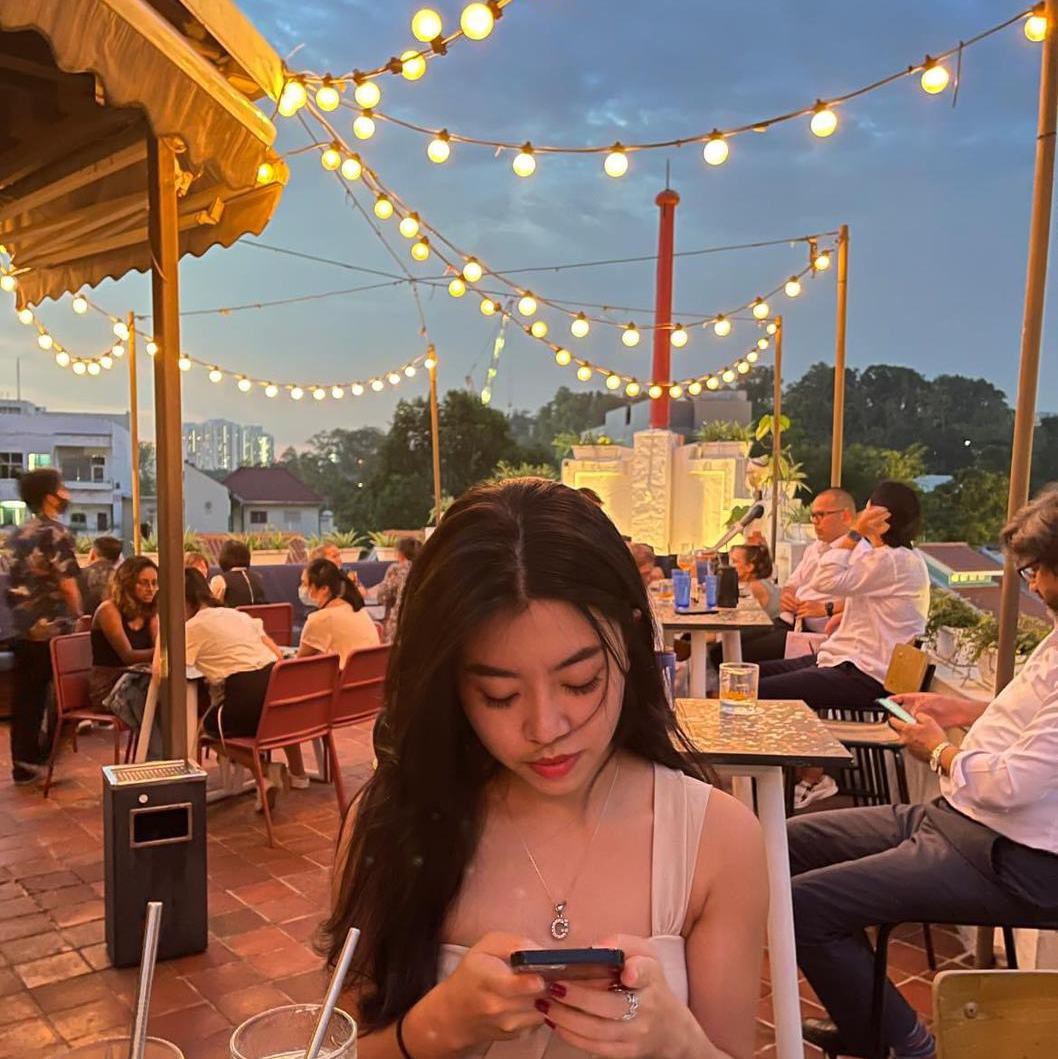 Young woman on a rooftop patio at dusk with string lights.