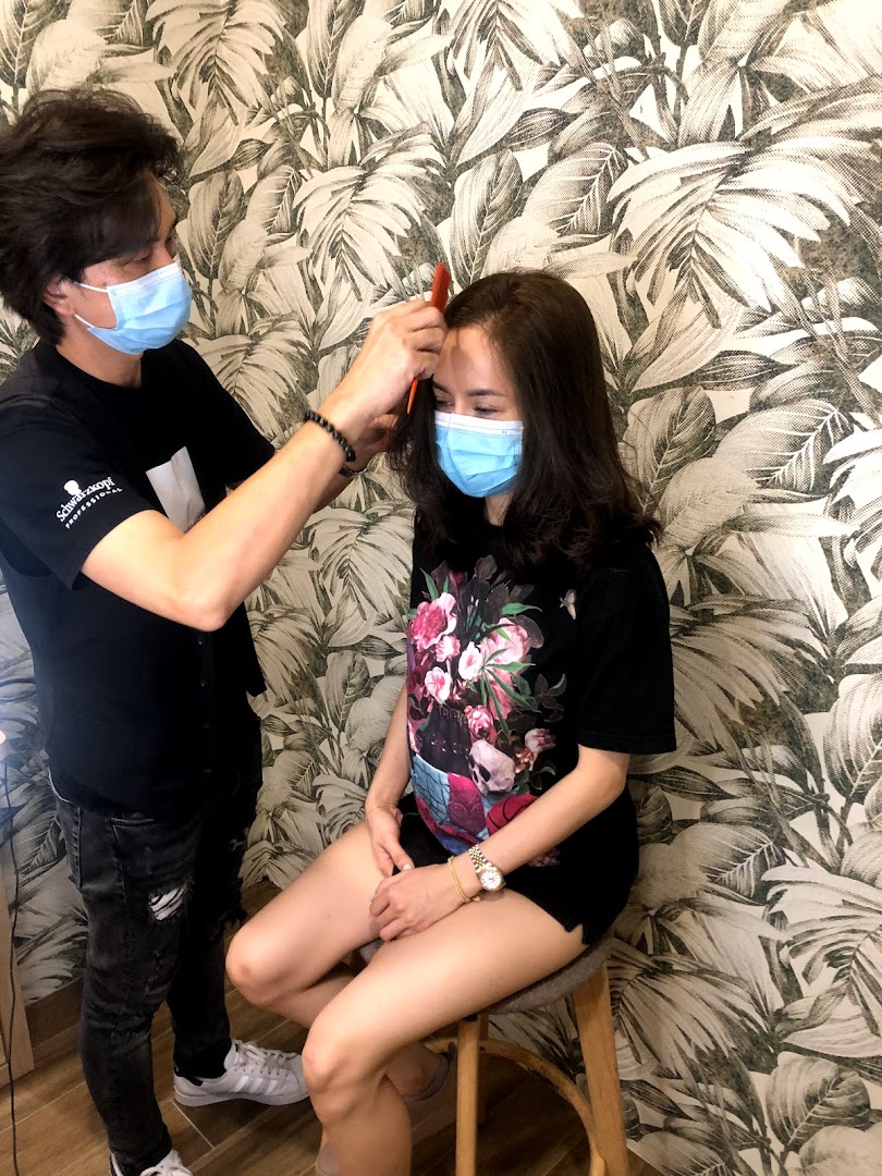 Stylist combs client's hair in a salon, both wearing masks.