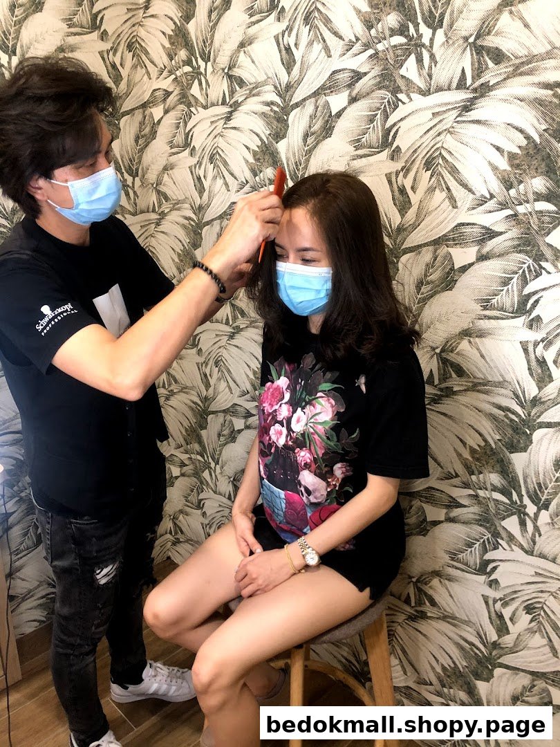 Stylist combs client's hair in a salon, both wearing masks.