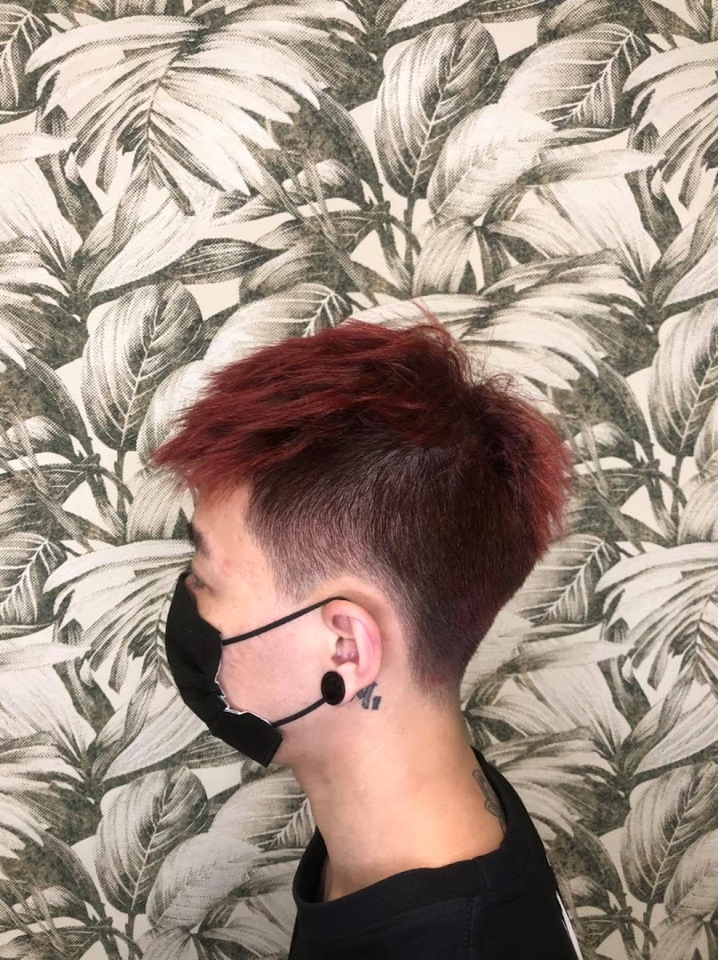 Person with red hair and fade haircut wearing a mask against leafy wallpaper.