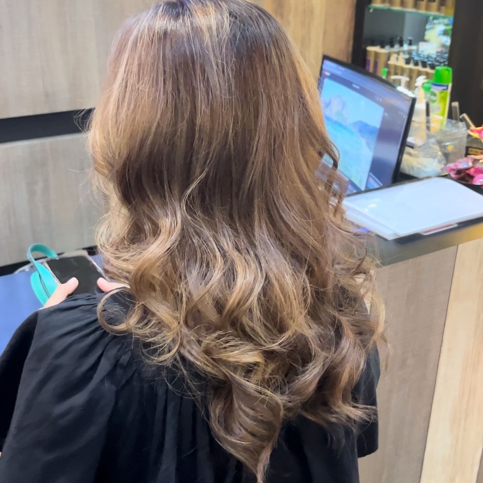 Back of person's head with long wavy hair in a salon setting.