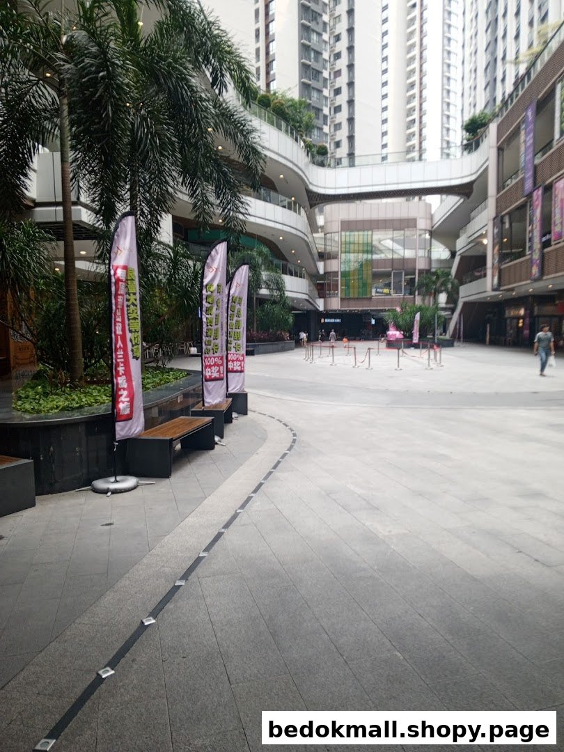 Outdoor plaza in front of a multi-story shopping complex with trees and flags.