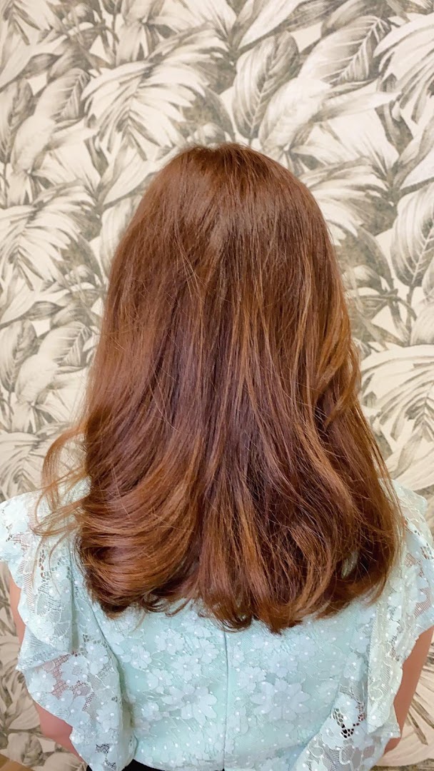 Back of a person with styled reddish-brown hair and a light blue top.