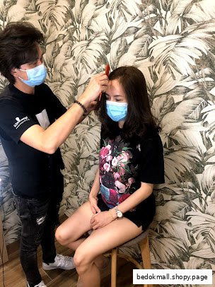 A stylist combs a client's hair inside a salon with patterned wallpaper.