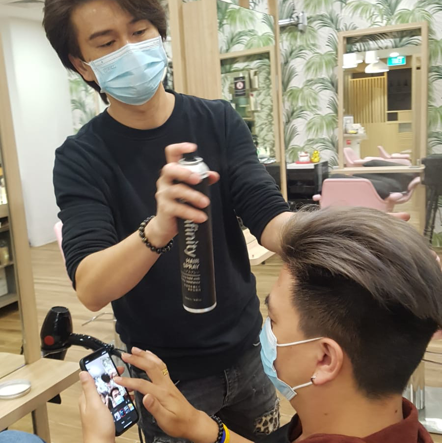 Hairdresser styling a client's hair with hairspray in a salon.