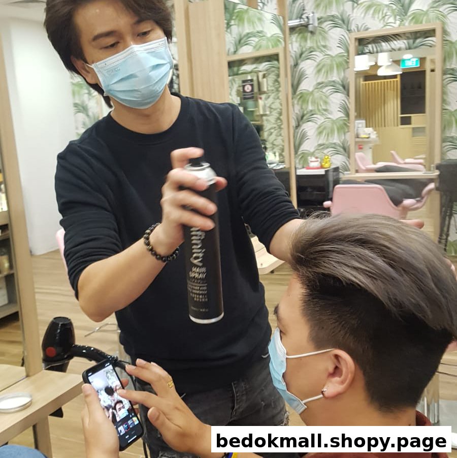 Hairdresser styling a client's hair with hairspray in a salon.