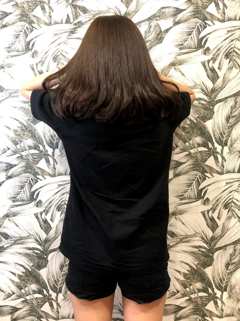 Person with long dark hair from behind, standing against a leafy wallpaper.