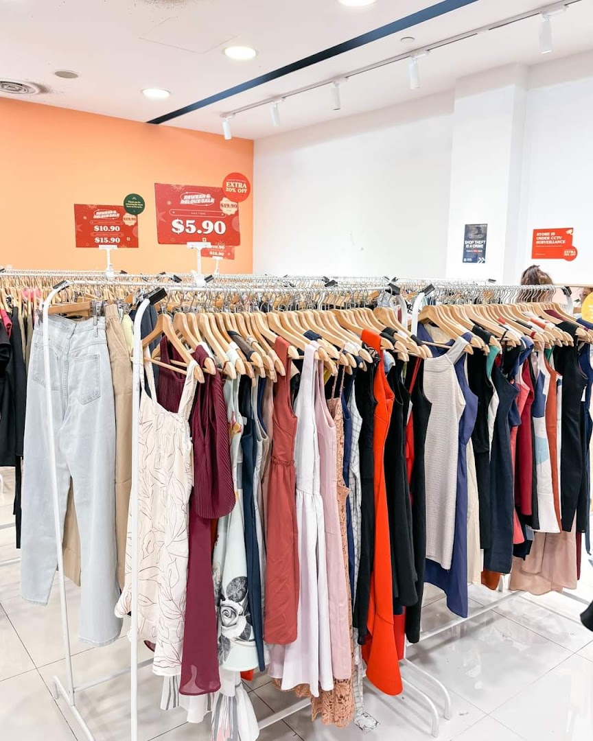 Interior view of a clothing store with racks of garments and sale signs.