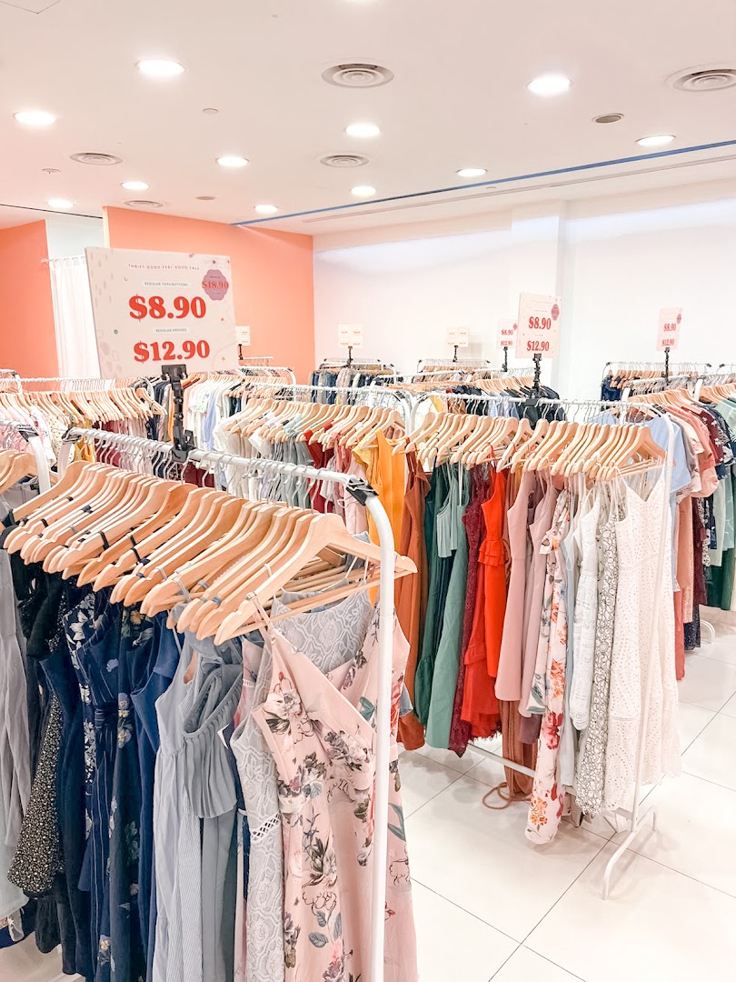 Interior view of a clothing store with many racks of garments and price signs.