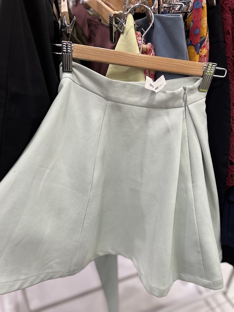 A light green skirt hangs on a wooden hanger in a clothing store.