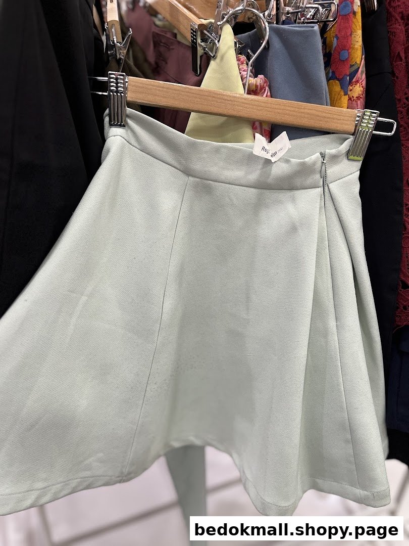 A light green skirt hangs on a wooden hanger in a clothing store.