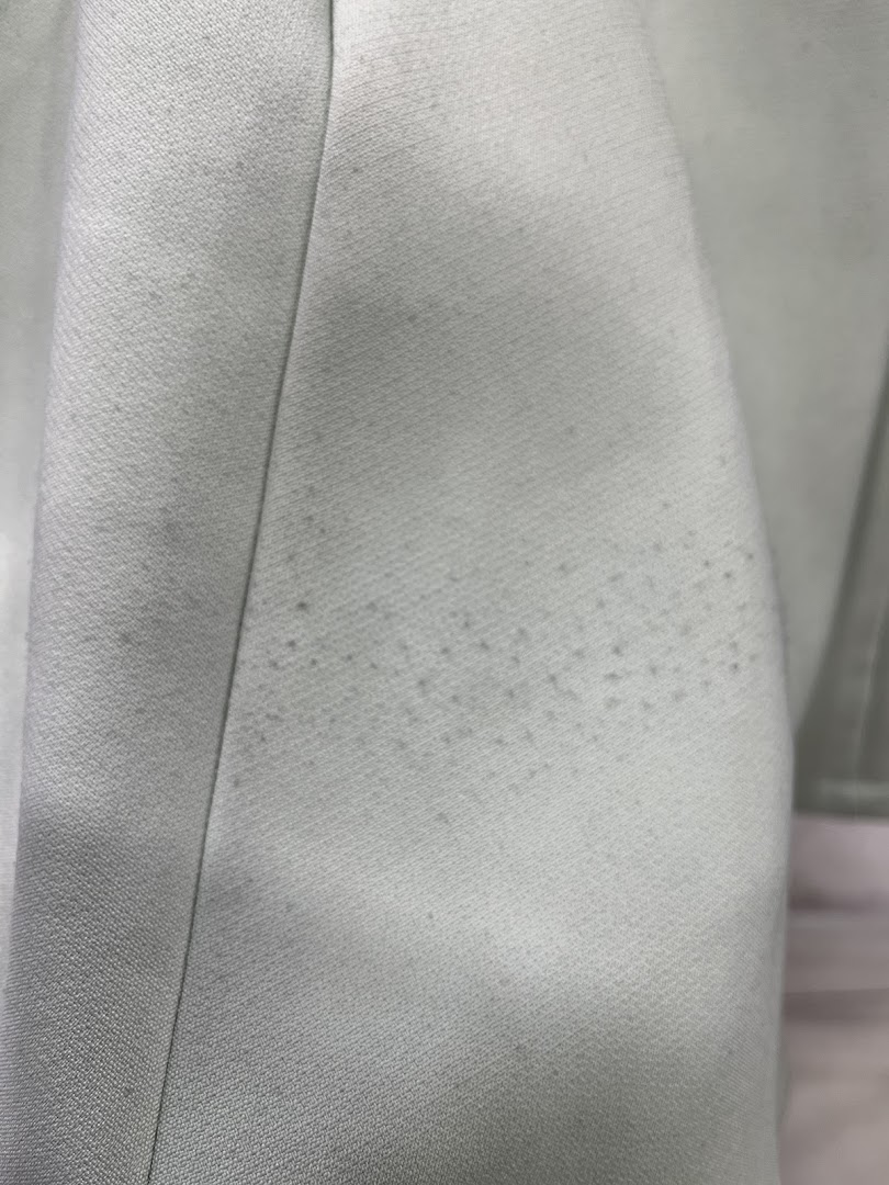 Close-up of light-colored fabric with small dark spots or stains.