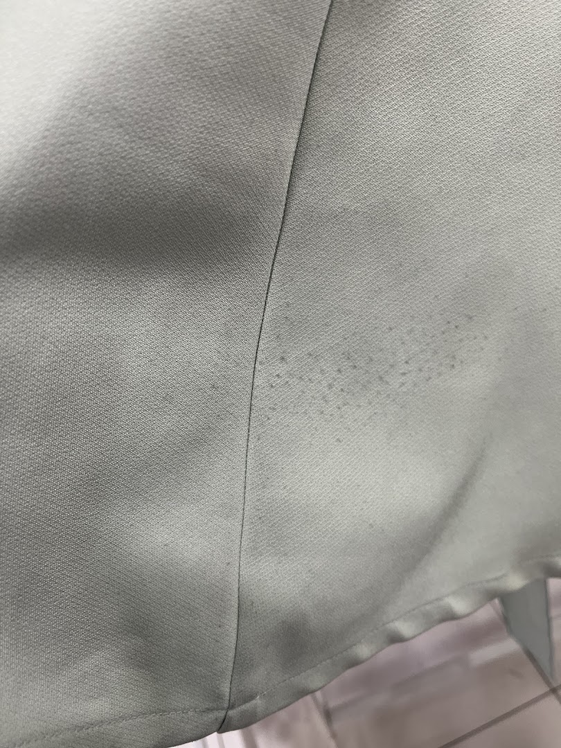 Close-up of light fabric with a seam and small dark spots.