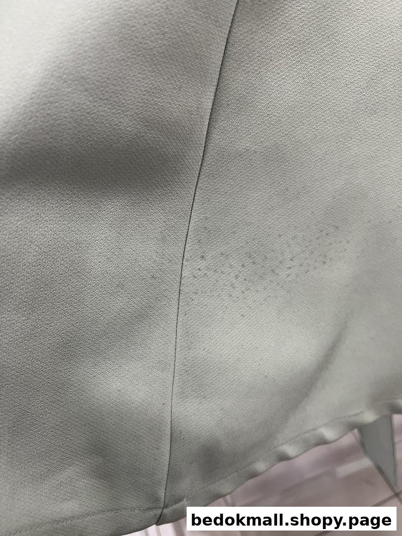 Close-up of light fabric with a seam and small dark spots.