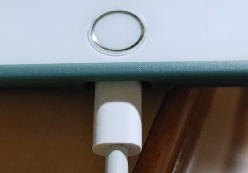 Close-up of a device charging with a white cable, home button visible.