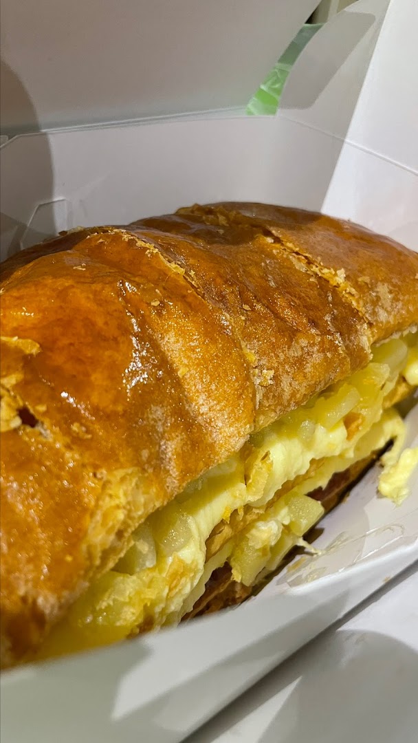 Close-up of a golden-brown pastry with creamy filling and apple chunks in a white box.