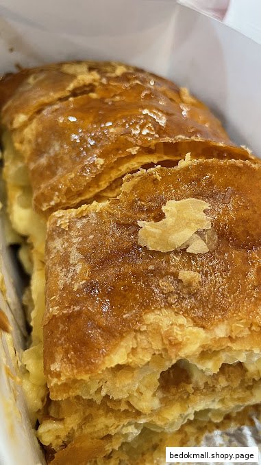 Close-up of a golden-brown, flaky apple strudel in a white box.