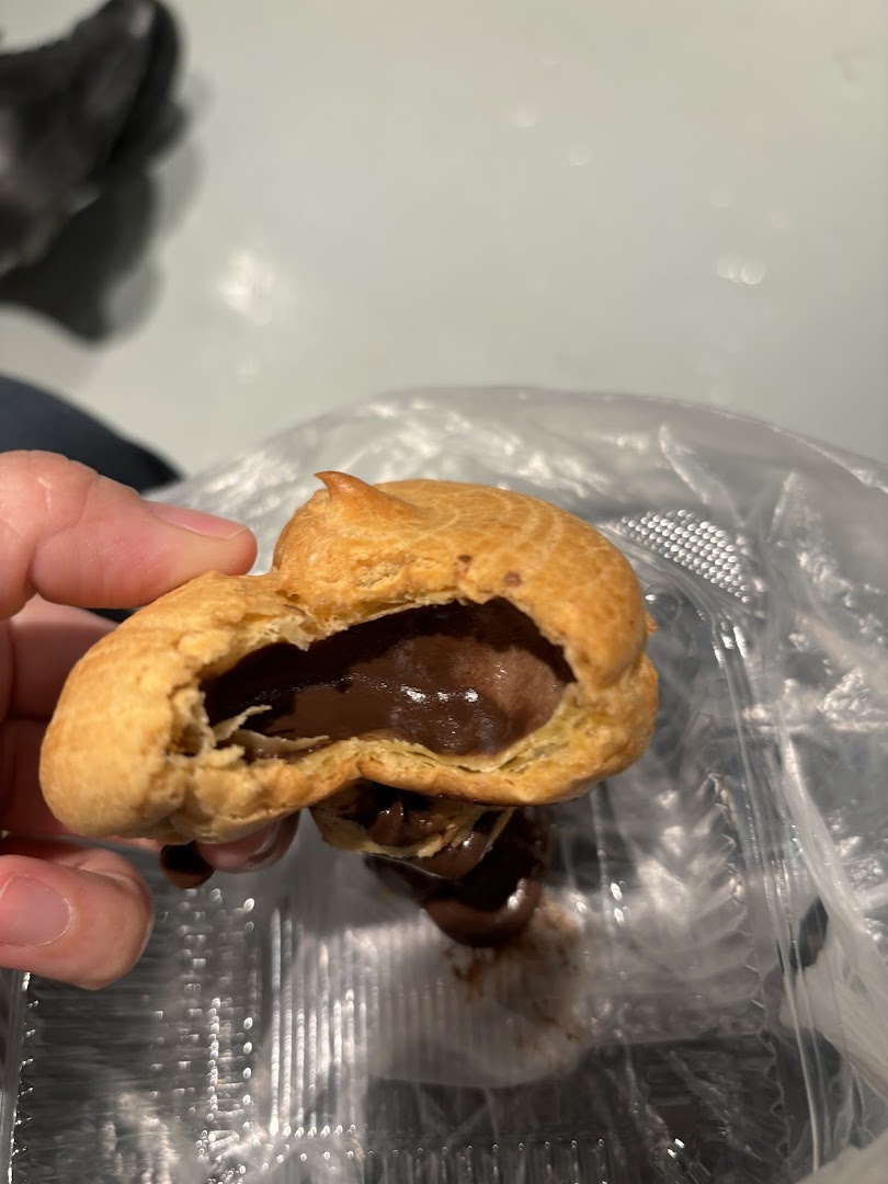 Hand holding a chocolate-filled cream puff over a plastic container.