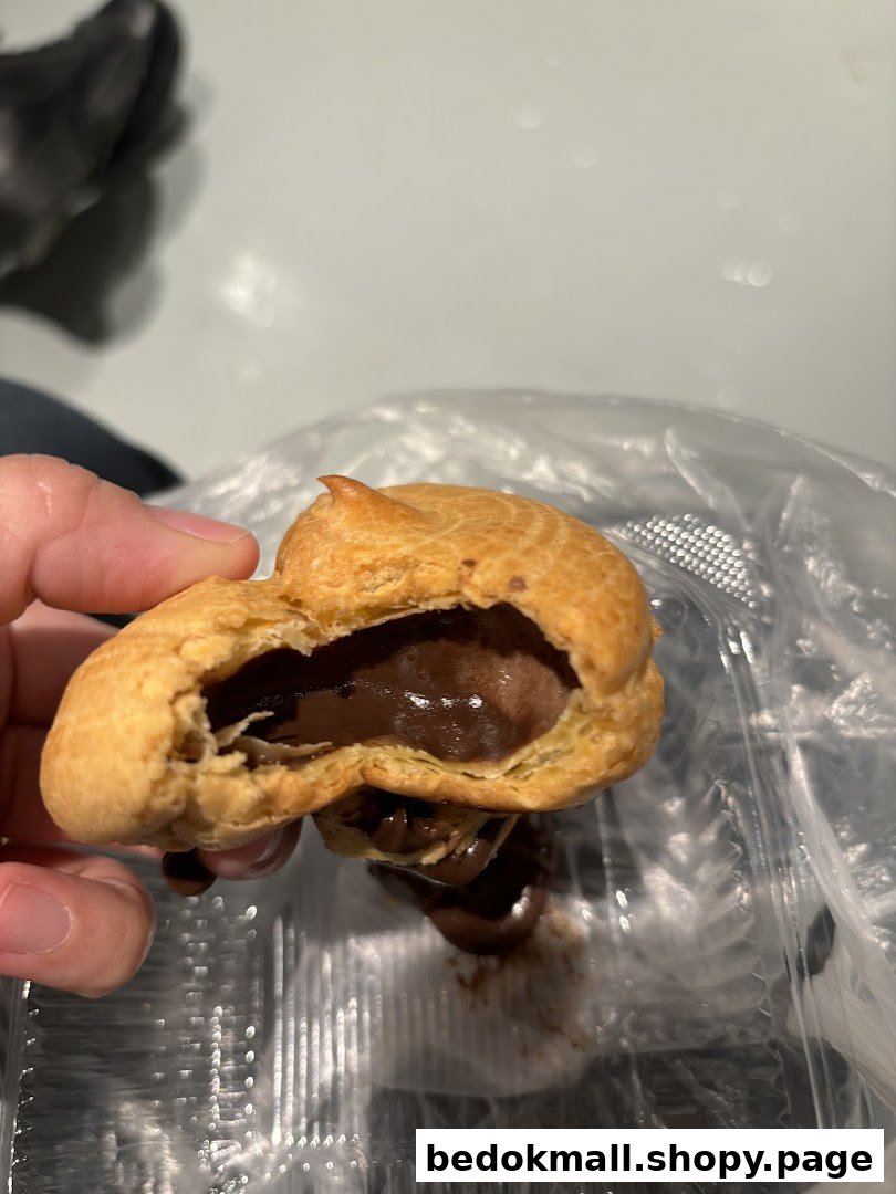 Hand holding a chocolate-filled cream puff over a plastic container.