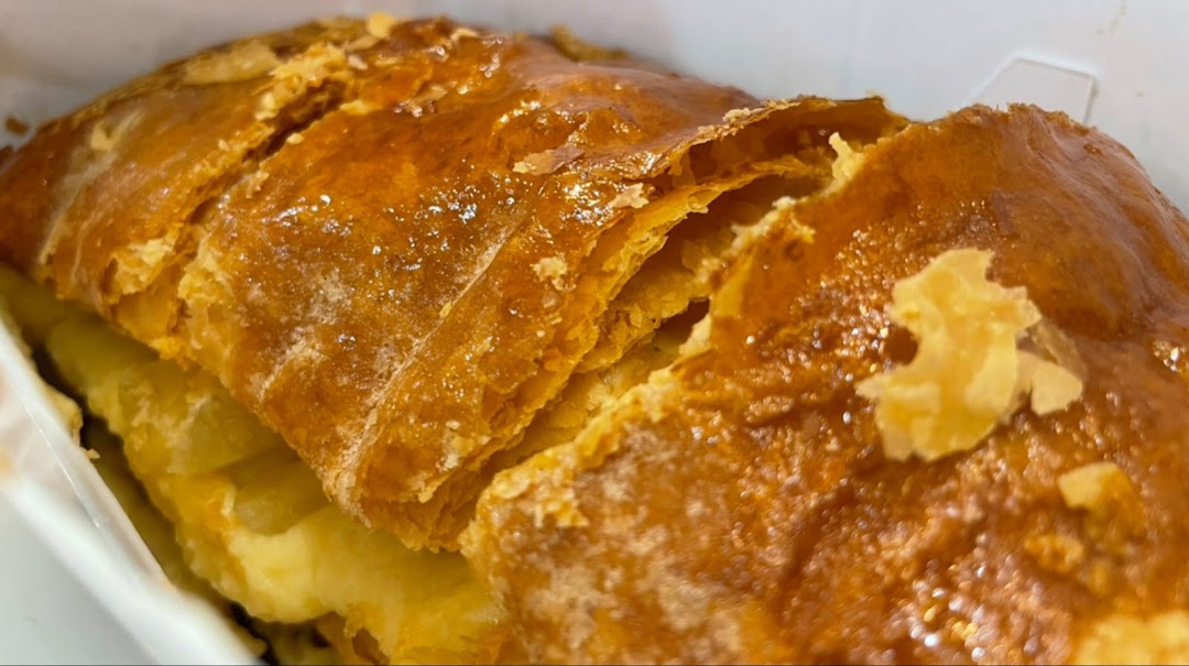 A close-up shot of a golden-brown, flaky apple strudel in a white container.