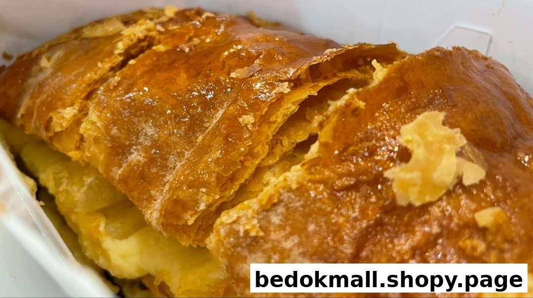 A close-up shot of a golden-brown, flaky apple strudel in a white container.