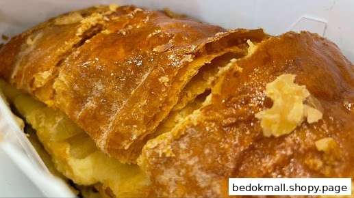 Close-up of a golden-brown, flaky pastry, likely an apple strudel, in a white container.