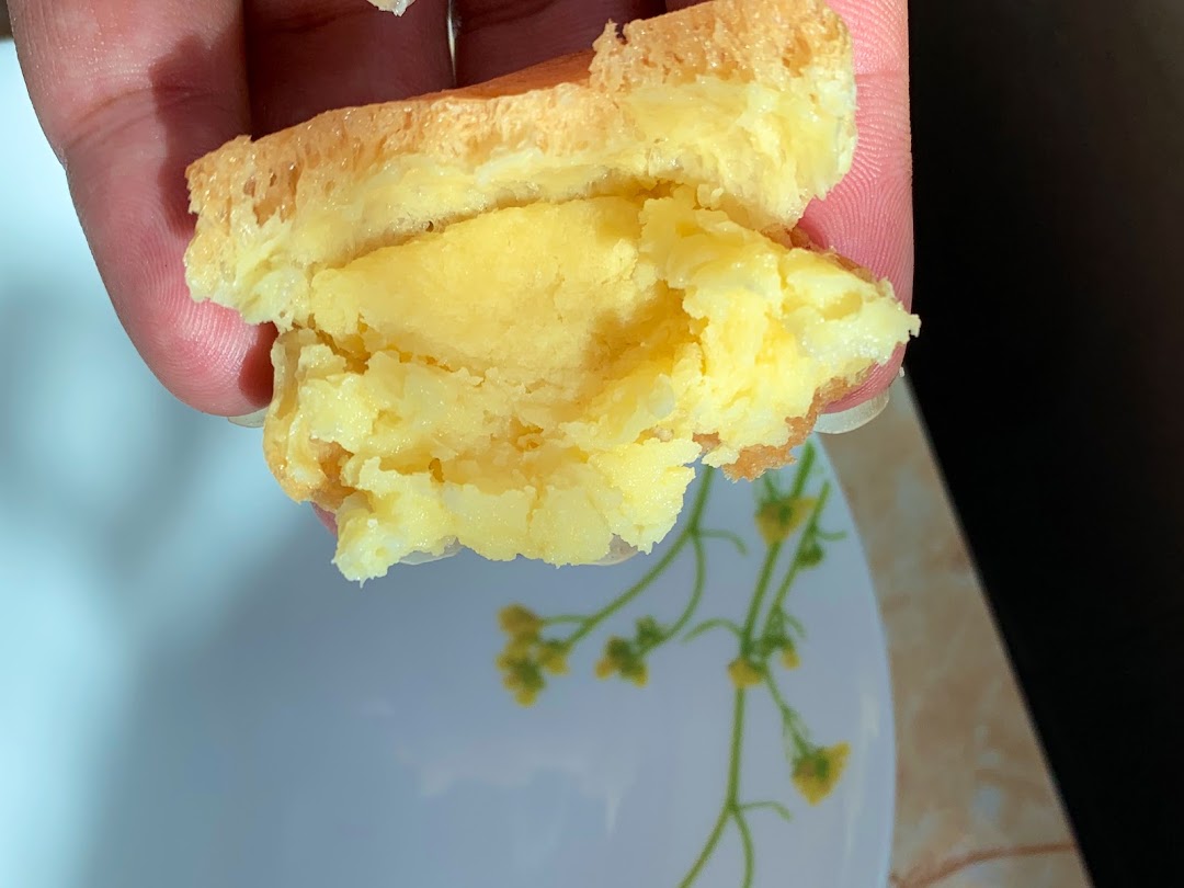 Hand holding a pastry with creamy yellow filling over a plate.