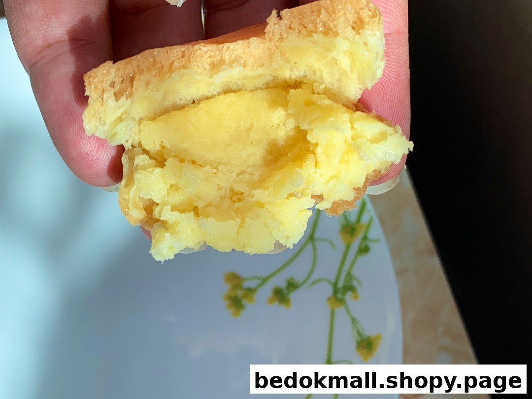 Hand holding a pastry with creamy yellow filling over a plate.