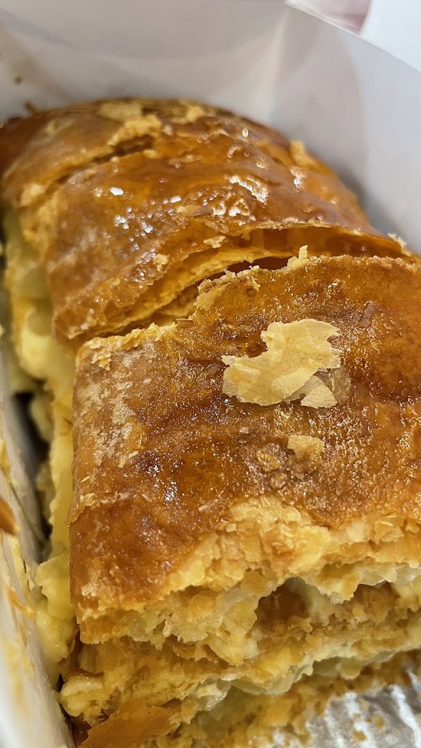 Close-up of a golden-brown, flaky pastry (apple strudel) in a white box.